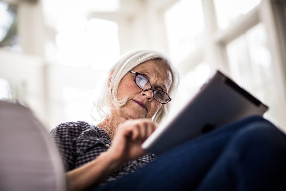 En äldre kvinna som sitter och surfar på sin iPad.