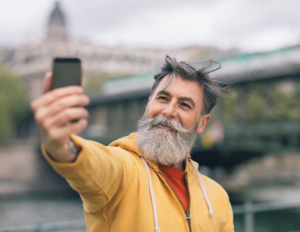 En glad pensionär med färgglada kläder som tar en selfie i Paris.