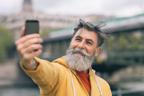 En glad pensionär med färgglada kläder som tar en selfie i Paris.